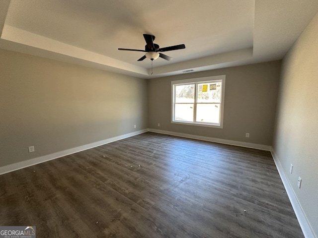 empty room with dark hardwood / wood-style floors, ceiling fan, and a raised ceiling