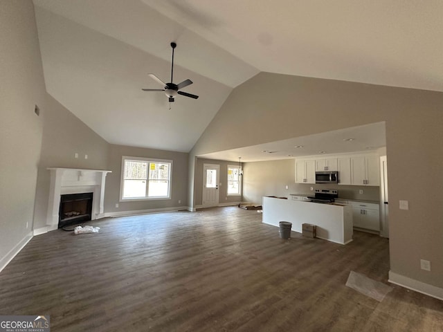 unfurnished living room with ceiling fan with notable chandelier, dark wood-type flooring, and vaulted ceiling