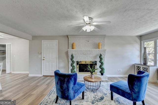 living room with a fireplace, a textured ceiling, ceiling fan, and light hardwood / wood-style flooring