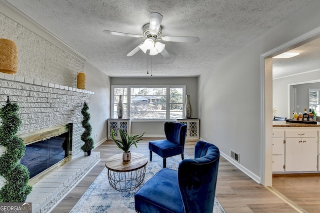 living area featuring light hardwood / wood-style floors, ceiling fan, a brick fireplace, and crown molding