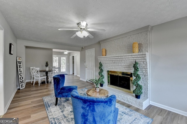 living room featuring a textured ceiling, french doors, hardwood / wood-style floors, a fireplace, and ceiling fan