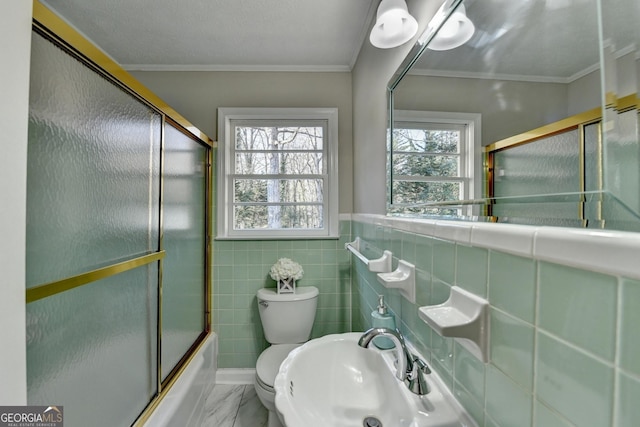 full bathroom with sink, tile walls, ornamental molding, toilet, and combined bath / shower with glass door