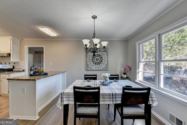 dining room featuring a notable chandelier, light wood-type flooring, crown molding, and a textured ceiling