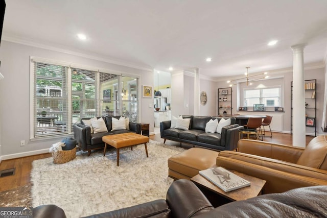 living room with hardwood / wood-style floors, a notable chandelier, ornamental molding, and decorative columns