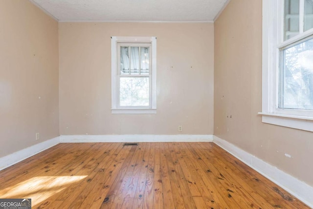 empty room with a textured ceiling, light hardwood / wood-style flooring, and crown molding