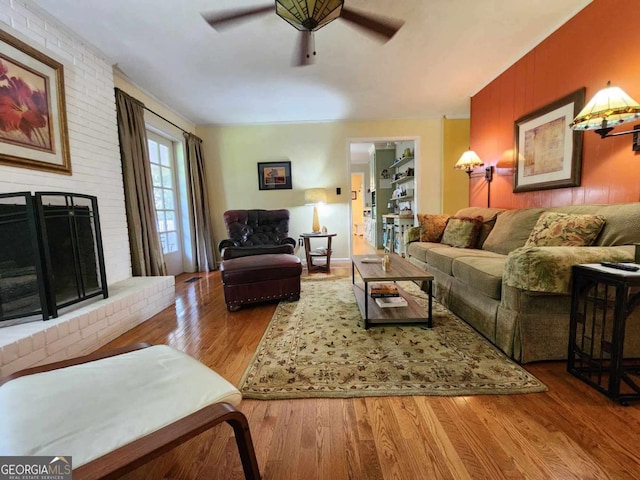 living room featuring ceiling fan, hardwood / wood-style floors, and a brick fireplace