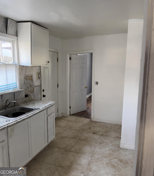 kitchen featuring light stone counters, white cabinetry, backsplash, and sink