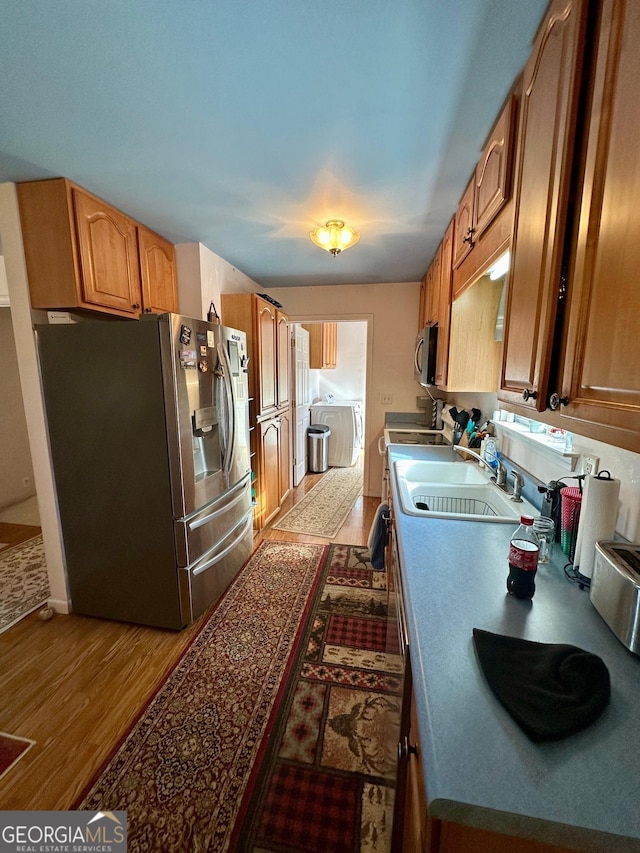 kitchen featuring sink, hardwood / wood-style flooring, washer and clothes dryer, and appliances with stainless steel finishes