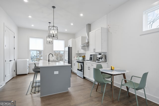 kitchen featuring stainless steel range, sink, wall chimney range hood, a center island with sink, and white cabinets