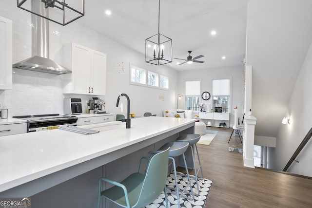 kitchen with range, wall chimney range hood, ceiling fan, decorative light fixtures, and white cabinetry