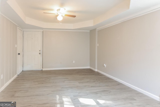 spare room with a tray ceiling, ceiling fan, and light hardwood / wood-style floors