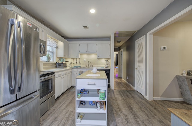 kitchen with stainless steel appliances, wood finished floors, light countertops, and white cabinets