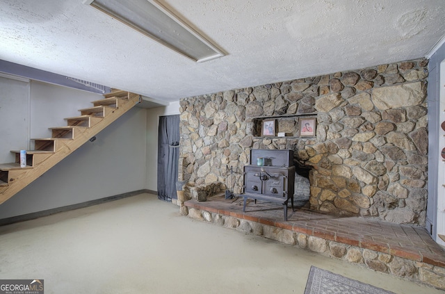 finished below grade area featuring a wood stove, stairs, baseboards, and a textured ceiling