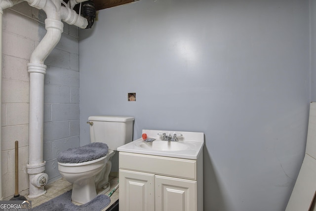 half bathroom featuring toilet, concrete block wall, and vanity