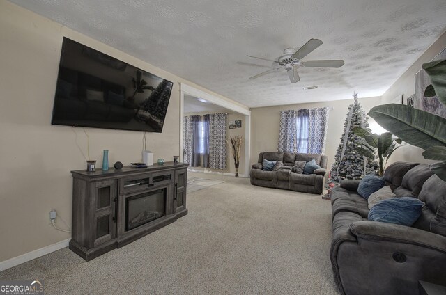 living area with a textured ceiling, ceiling fan, baseboards, carpet, and a glass covered fireplace