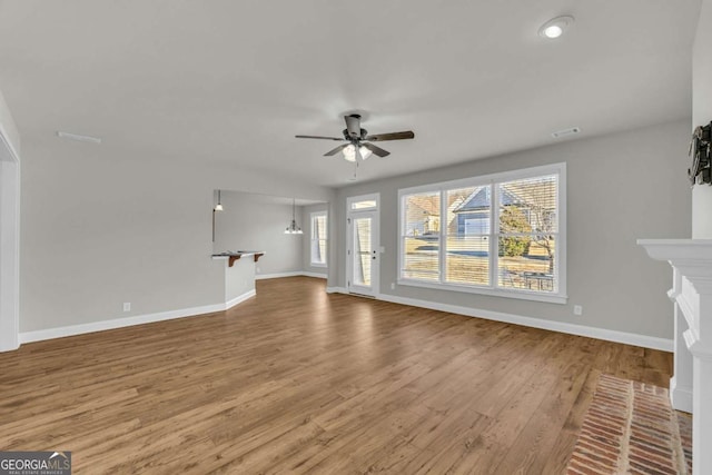 unfurnished living room with a brick fireplace, wood-type flooring, and ceiling fan