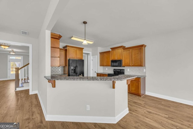 kitchen with black appliances, a kitchen breakfast bar, dark stone countertops, and tasteful backsplash