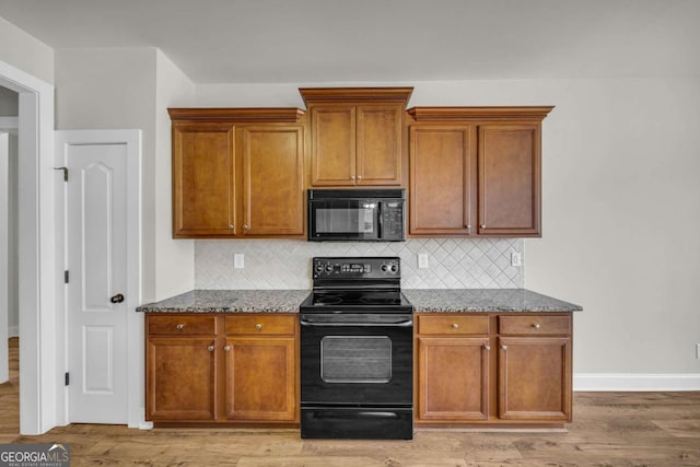 kitchen with dark stone countertops, light hardwood / wood-style floors, tasteful backsplash, and black appliances