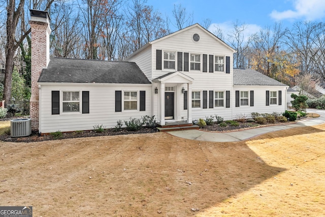 view of front of home featuring central AC unit, a chimney, a front yard, and a shingled roof