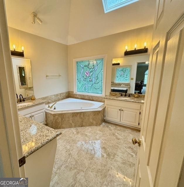 bathroom featuring vanity, a skylight, a wealth of natural light, and tiled tub