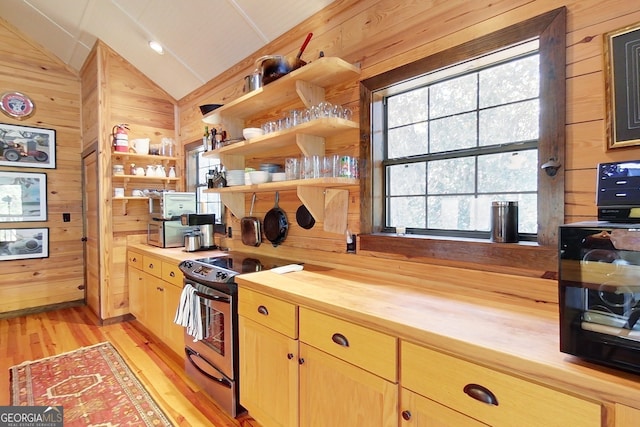 kitchen featuring electric range, butcher block counters, light hardwood / wood-style floors, lofted ceiling, and wood walls