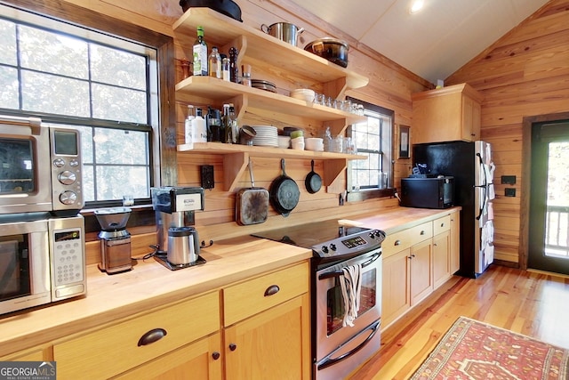 kitchen featuring lofted ceiling, wooden walls, butcher block countertops, plenty of natural light, and stainless steel appliances