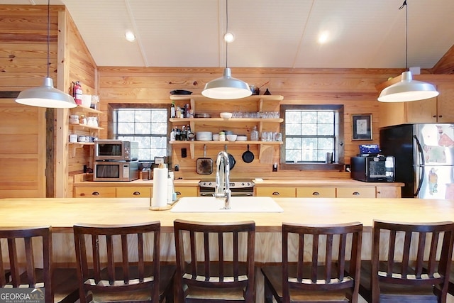 kitchen featuring a healthy amount of sunlight, wooden walls, a breakfast bar area, and hanging light fixtures