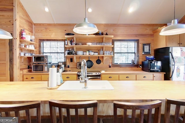 kitchen featuring black fridge, wood walls, a breakfast bar, and decorative light fixtures