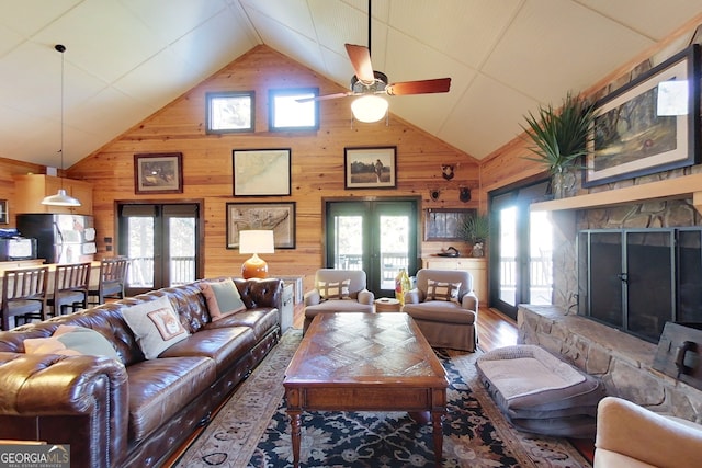 living room with a fireplace, wood walls, french doors, and ceiling fan