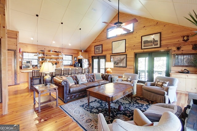 living room featuring ceiling fan, light wood-type flooring, and wooden walls