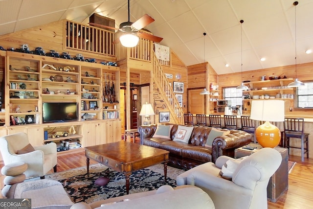 living room with light hardwood / wood-style floors, high vaulted ceiling, ceiling fan, and wooden walls