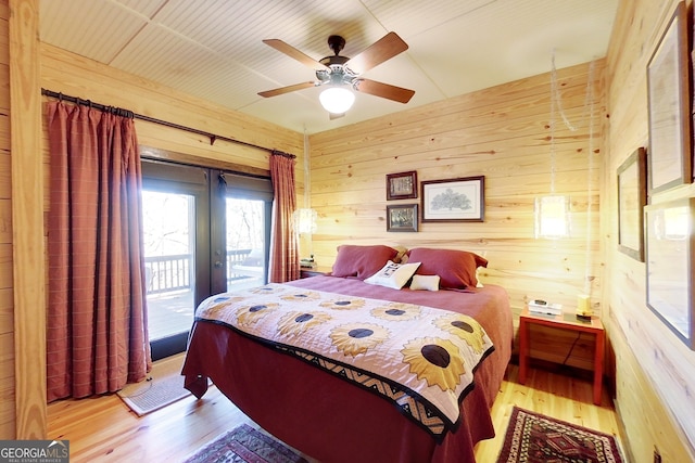 bedroom with light wood-type flooring, access to outside, ceiling fan, and wood walls