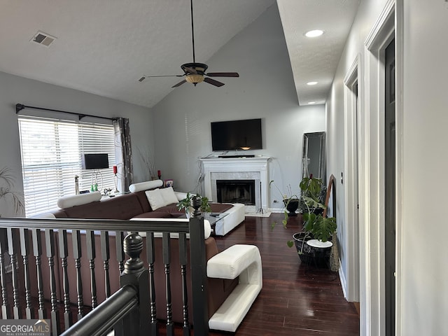 living room featuring dark wood-type flooring, vaulted ceiling, ceiling fan, a premium fireplace, and a textured ceiling