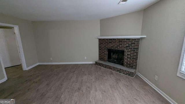 unfurnished living room featuring hardwood / wood-style flooring and a brick fireplace