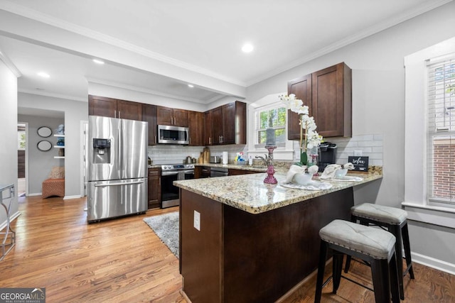 kitchen with stainless steel appliances, light hardwood / wood-style flooring, kitchen peninsula, decorative backsplash, and ornamental molding