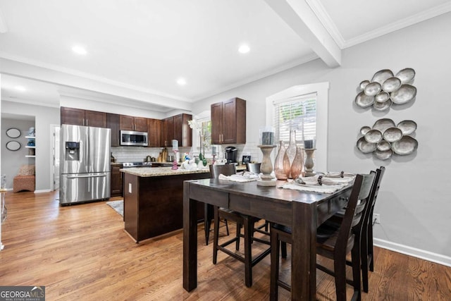 kitchen featuring crown molding, light wood-type flooring, appliances with stainless steel finishes, a kitchen island, and dark brown cabinetry