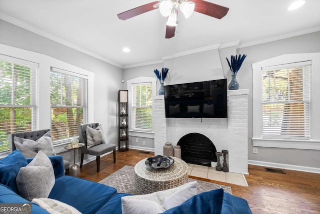 living room featuring hardwood / wood-style flooring, ceiling fan, crown molding, and a brick fireplace