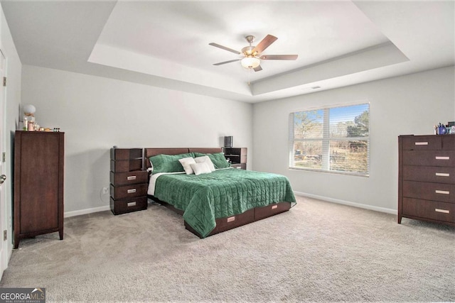 bedroom featuring ceiling fan, light colored carpet, and a tray ceiling