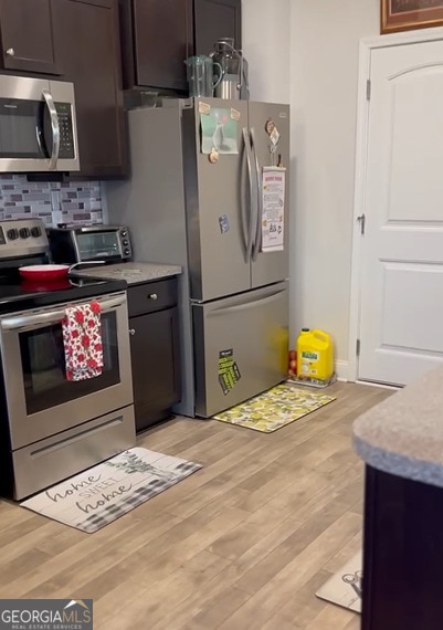 kitchen with decorative backsplash, dark brown cabinets, light hardwood / wood-style flooring, and appliances with stainless steel finishes