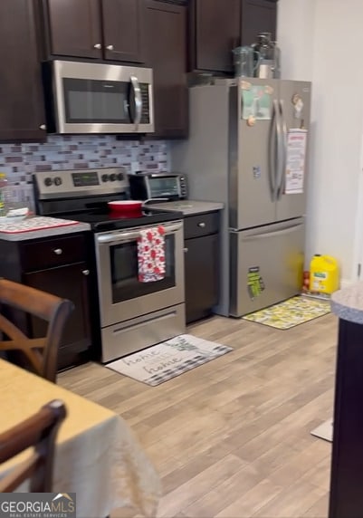 kitchen with backsplash, dark brown cabinets, light wood-type flooring, and appliances with stainless steel finishes