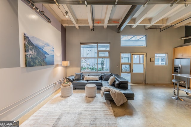 living area with finished concrete floors, a wealth of natural light, beamed ceiling, and a towering ceiling