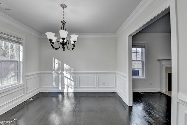 unfurnished dining area featuring a premium fireplace, crown molding, dark hardwood / wood-style flooring, and a chandelier