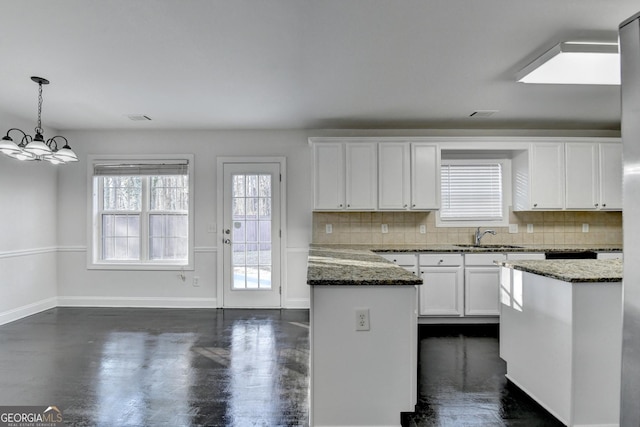 kitchen featuring a center island, dark stone counters, decorative backsplash, decorative light fixtures, and white cabinetry