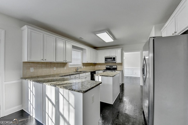 kitchen with dark stone counters, white cabinets, sink, a kitchen island, and stainless steel appliances