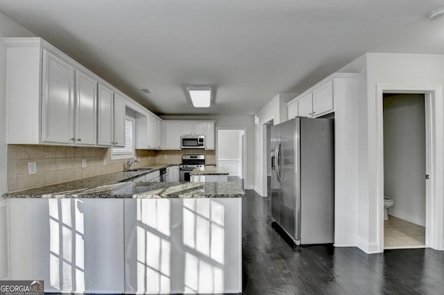 kitchen with kitchen peninsula, dark stone counters, stainless steel appliances, sink, and white cabinets