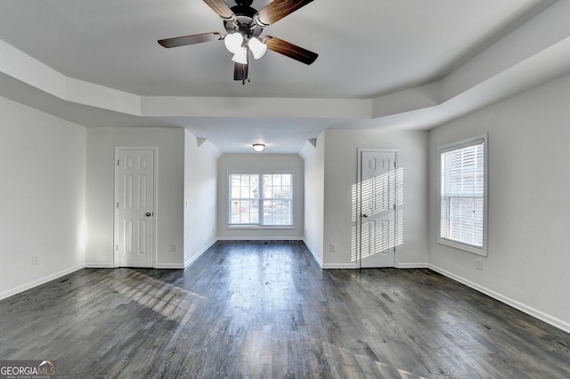 empty room with a tray ceiling, dark hardwood / wood-style floors, and a healthy amount of sunlight