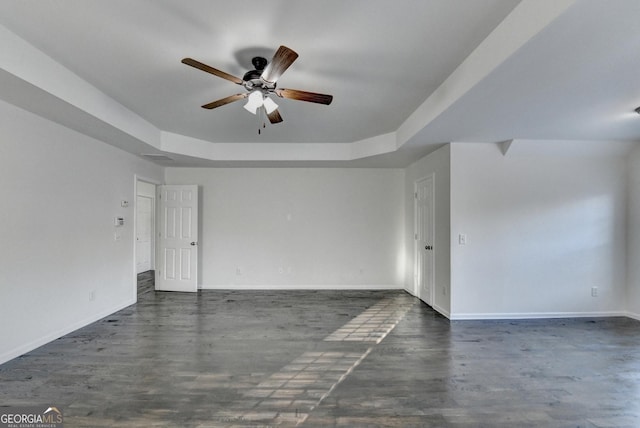 unfurnished room with ceiling fan, dark hardwood / wood-style floors, and a tray ceiling