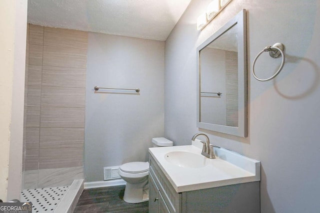 bathroom with vanity, a textured ceiling, tiled shower, hardwood / wood-style floors, and toilet