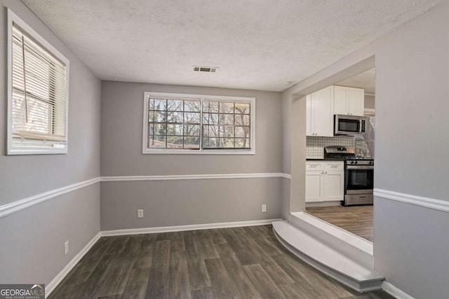 kitchen featuring decorative backsplash, dark hardwood / wood-style floors, a textured ceiling, white cabinetry, and stainless steel appliances