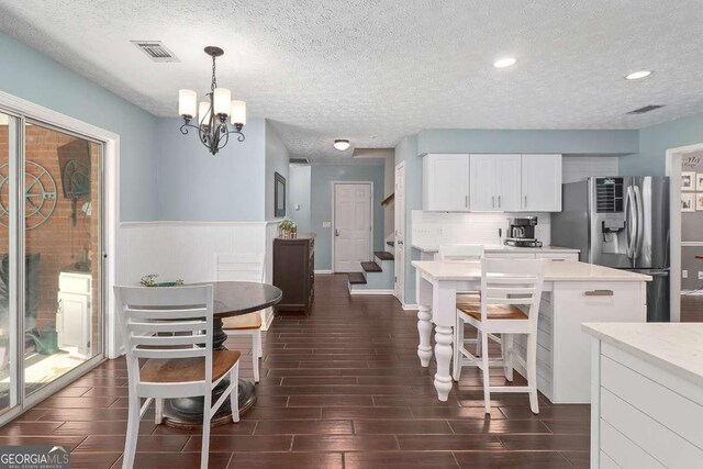 kitchen with white cabinetry, stainless steel fridge, pendant lighting, a textured ceiling, and a kitchen island